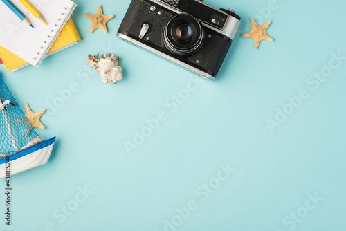 Top view photo of notebooks pencils camera ship toy seashell starfishes and camera on isolated pastel blue background with copyspace