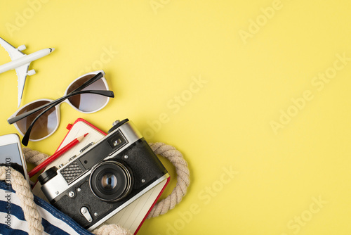 Overhead photo of sunglasses phone bag camera notebook pencil and plane isolated on the yellow background with copyspace