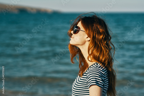 red-haired woman in sunglasses on the beach near the blue sea and mountains in the background