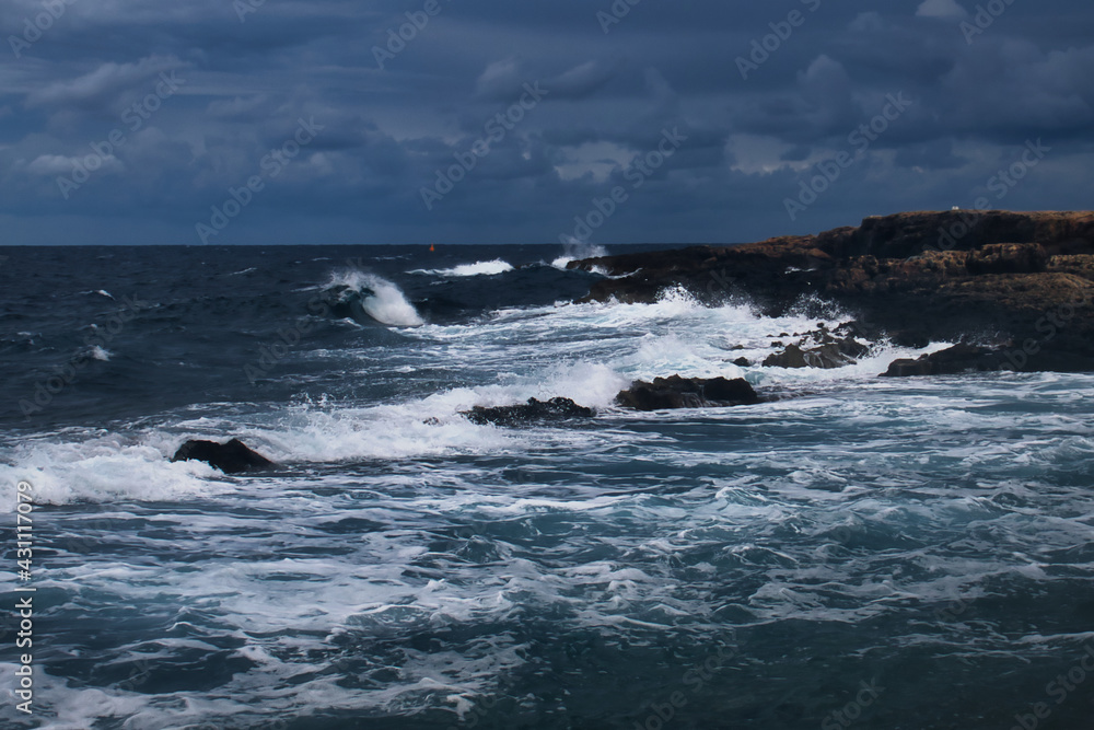 Wave in the ocean as water splashes on rocky shore on a stormy day in Qawra, Malta.