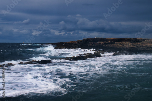 White foam and waves in the blue ocean at a rocky beach in Qawra, Malta on a stormy day.
