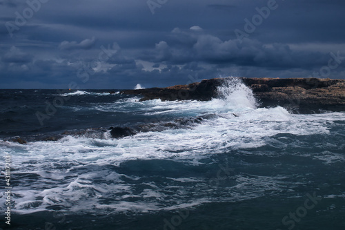 Wave crashing against rocks on a beach in Qawra, Malta on a stormy day.
