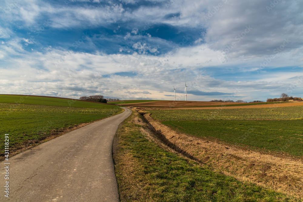 Rural landscape with road, fields, meadows, small forest, wind farm and blue sky with clouds