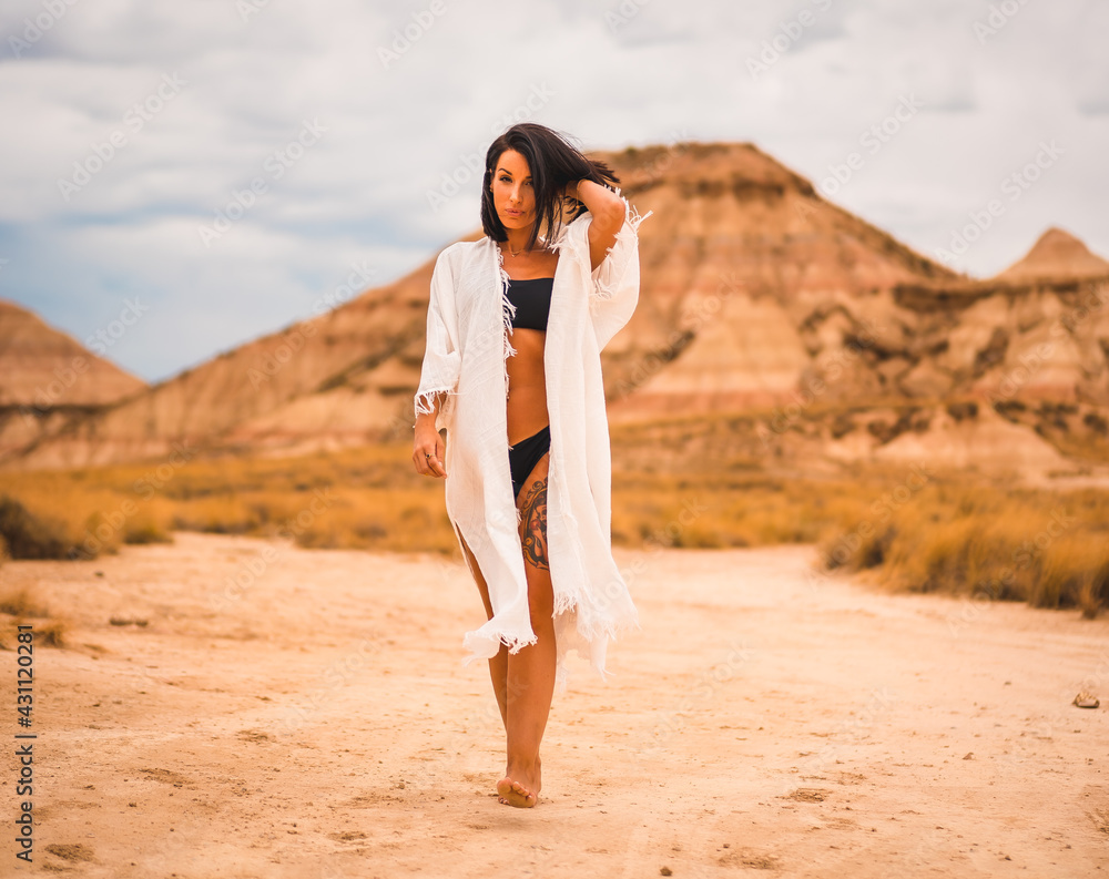 A young brunette Caucasian girl in a white dress and a black bikini walking barefoot through a desert A young brunette Caucasian girl in a white dress and a black bikini walking barefoot through a desert