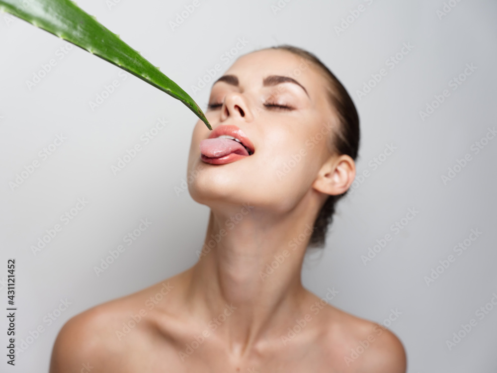 woman with closed eyes touching tongue to aloe leaf on light woman with closed eyes touching tongue to aloe leaf on light
