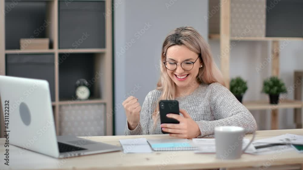 Happy business woman receiving good news message making winner gesture use smartphone at workplace Happy business woman receiving good news message making winner gesture use smartphone at workplace