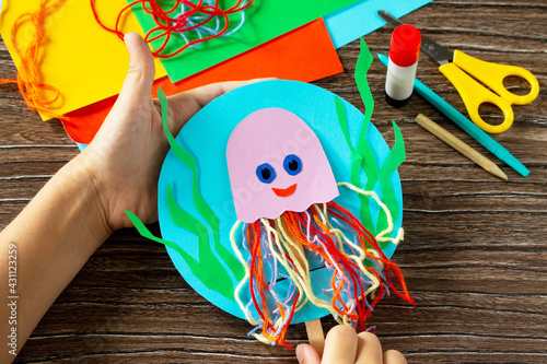 The child is holding puppet stics toy octopus on a wooden table. Handmade. Childrens creativity project, crafts for kids. photo