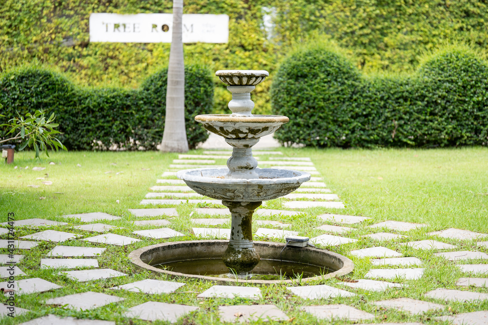 The fountain in the middle of the garden has a stone walkway surrounding it.