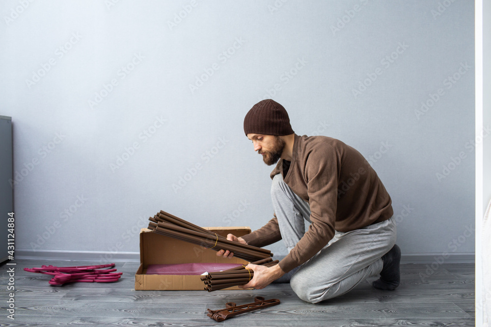 bearded man unpacks a box of furniture parts.