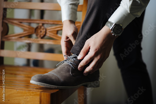 Groom straightens the laced laces with his foot on the chair