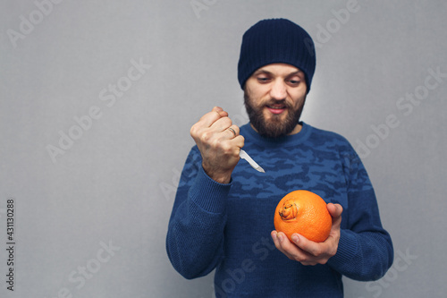 angry bearded man wants to cut out a large navel of an orange with a scalpel, the concept of hemorrhoids or proctological diseases. photo