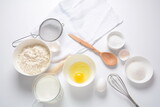 Frame of food ingredients for baking on a white background. Flour, eggs, sugar and milk in white and wooden bowls . Cooking and baking concept.