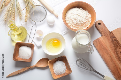 Frame of food ingredients for baking on a white background. Flour, eggs, sugar and milk in white and wooden bowls . Cooking and baking concept.