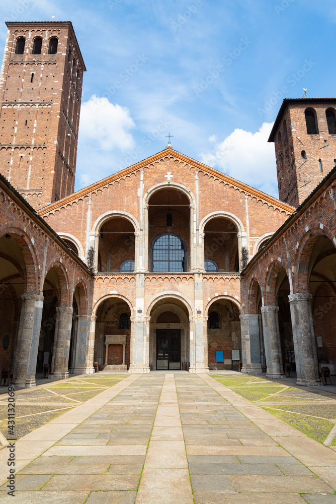 Patio of the famous Sant'Ambrogio (meaning Saint Ambrogio) romanesque cathedral in Milan, Italy, with beautiful facade with arches and bell towers. Blue sky on the background.