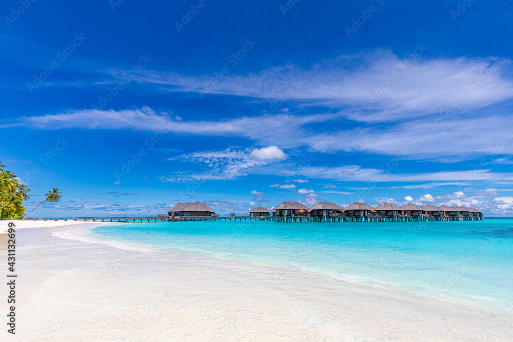 Island view of Maldives island, luxury water villas resort and wooden pier. Beautiful sky and ocean lagoon beach, palms sand. Summer vacation holiday and travel concept. Paradise shore coast landscape