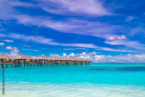 Island view of Maldives island, luxury water villas resort and wooden pier. Beautiful sky and ocean lagoon beach, palms sand. Summer vacation holiday and travel concept. Paradise shore coast landscape © icemanphotos