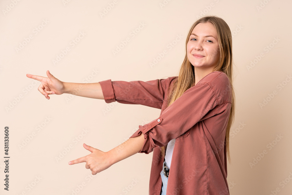 Teenager Ukrainian girl isolated on beige background pointing finger to the side and presenting a product