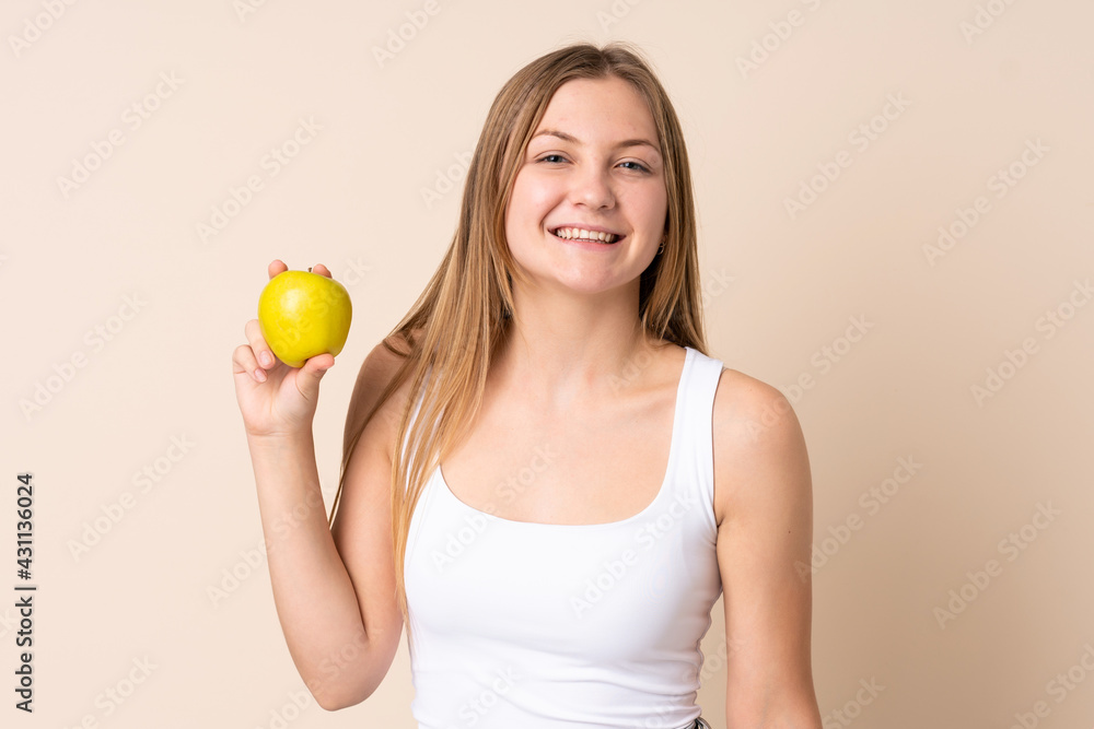 Teenager Ukrainian girl isolated on beige background with an apple and happy Teenager Ukrainian girl isolated on beige background with an apple and happy