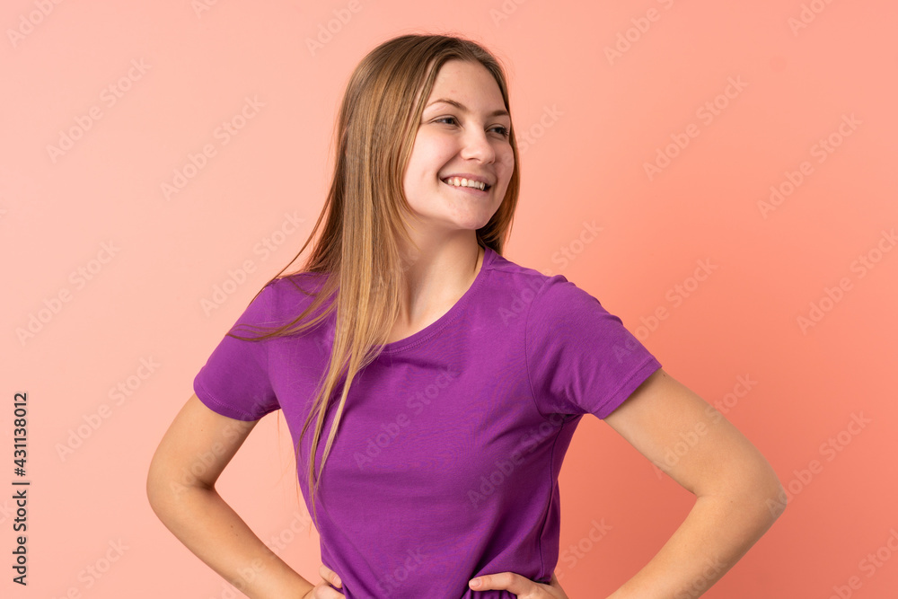 Fototapeta premium Teenager Ukrainian girl isolated on pink background posing with arms at hip and smiling