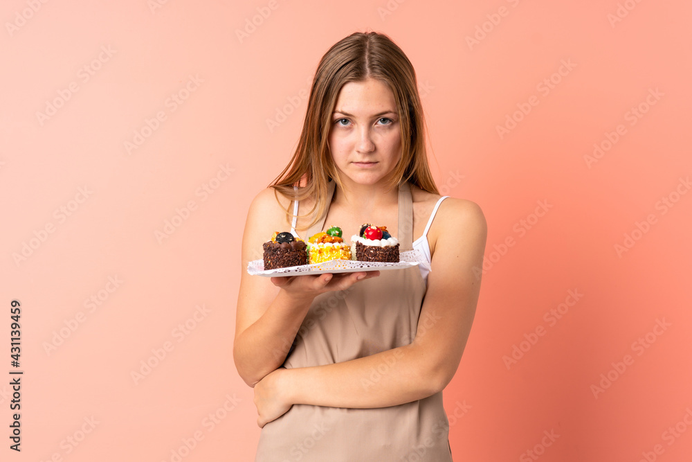 Pastry Ukrainian chef holding a muffins isolated on pink background keeping arms crossed Pastry Ukrainian chef holding a muffins isolated on pink background keeping arms crossed