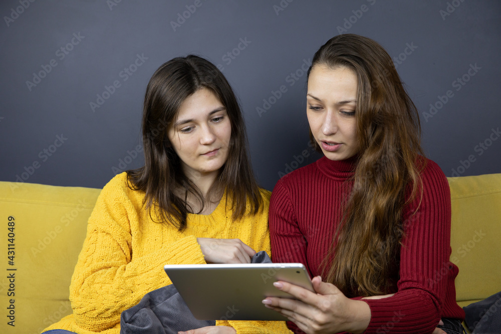 two pretty long-haired brunette girls make purchases or payments online, female millennial sit relax on yellow sofa at home using tablet and internet for Couch shopping on ecommerce site two pretty long-haired brunette girls make purchases or payments online, female millennial sit relax on yellow sofa at home using tablet and internet for Couch shopping on ecommerce site