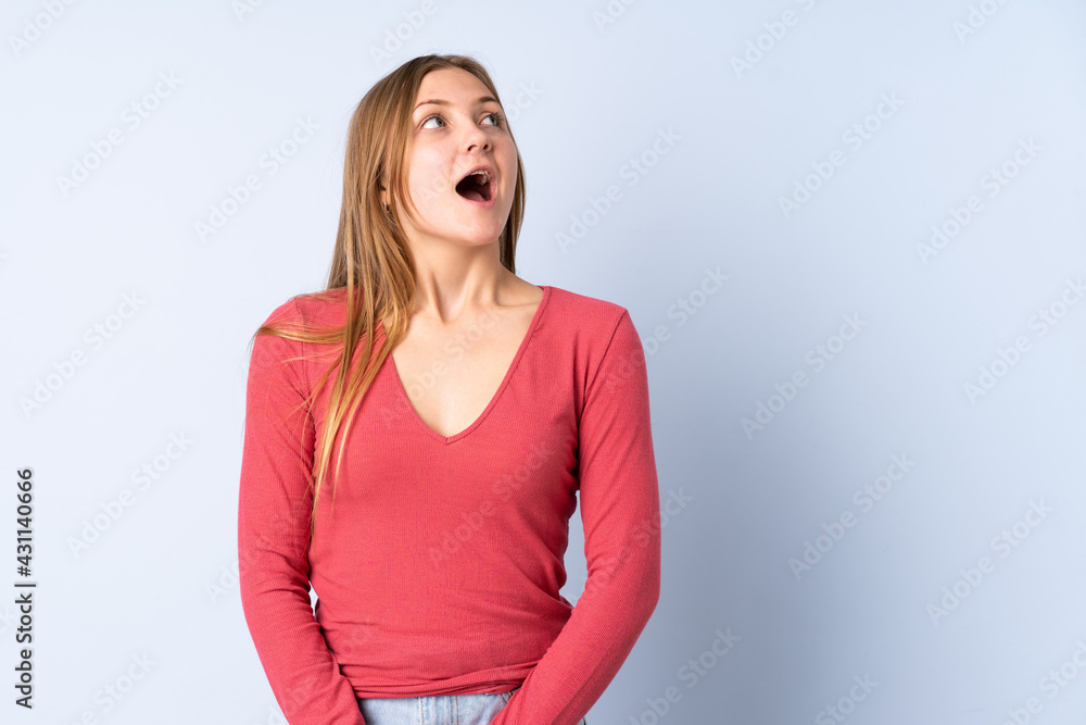 Teenager Ukrainian girl isolated on blue background looking up and with surprised expression Teenager Ukrainian girl isolated on blue background looking up and with surprised expression