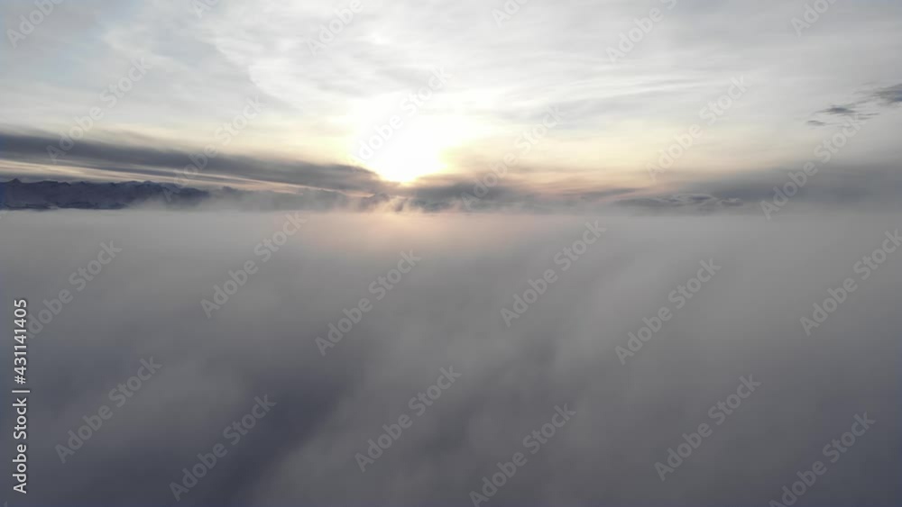 Incredible aerial view shot above swirling fog and clouds at sunset in the mountains. Flying over a low cloud surface with a ridge in the background Incredible aerial view shot above swirling fog and clouds at sunset in the mountains. Flying over a low cloud surface with a ridge in the background