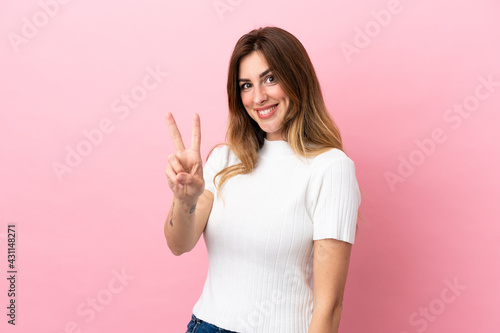 Caucasian woman isolated on pink background smiling and showing victory sign