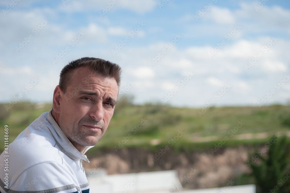 An attractive adult Caucasian man looking at the camera from a balcony with an unfocused background of sky and mountains