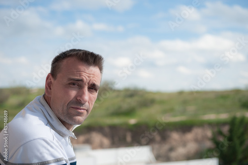 An attractive adult Caucasian man looking at the camera from a balcony with an unfocused background of sky and mountains