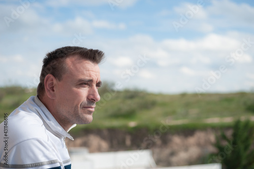An attractive adult Caucasian man looking at the horizon from a balcony with an unfocused background of sky and mountains