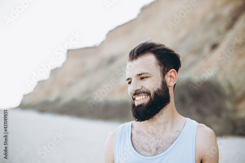 portrait of a stylish young man with a beard and a face on which the sea sand on the background of the sea shore