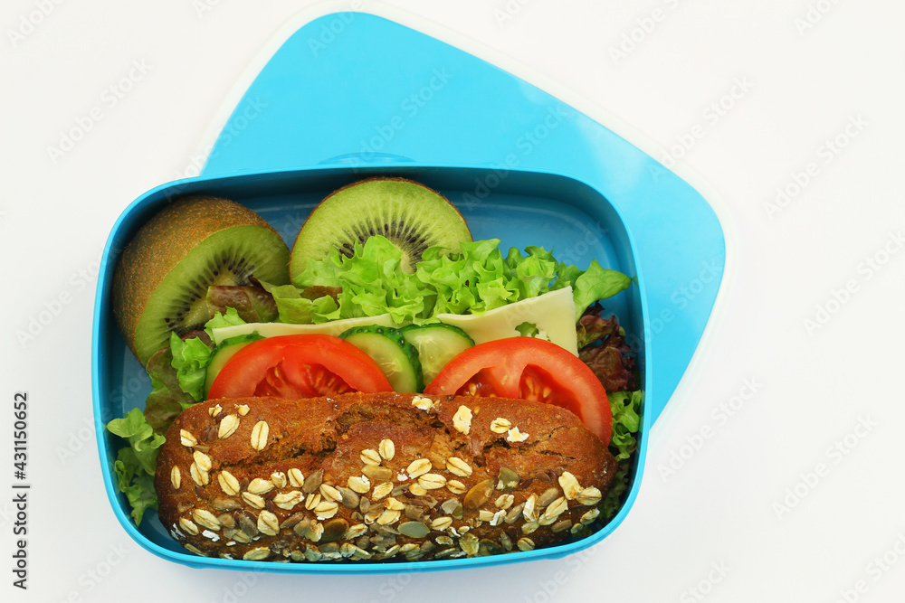 Whole grain oat roll with cheese, lettuce, cucumber, tomato and kiwi fruit in blue lunchbox on white background