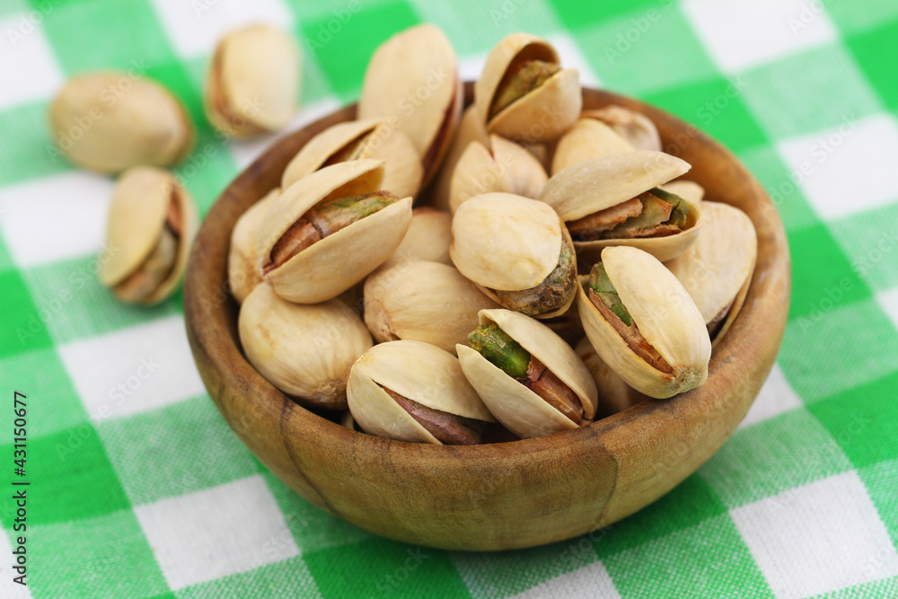 Pistachio nuts in wooden bowl on checkered cloth, closeup