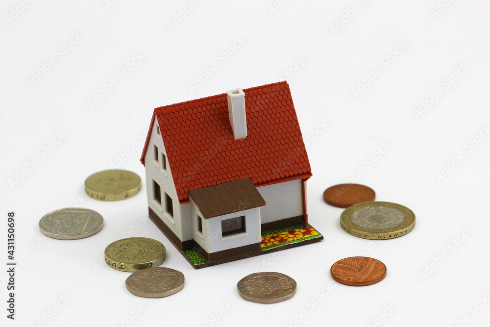 Model house with British coins scattered around it on white background