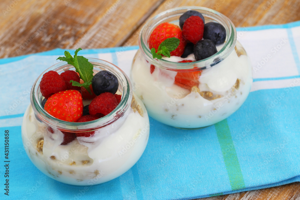 Nutritious breakfast: bio yoghurt with granola, fresh strawberries, raspberries and blueberries in transparent glasses