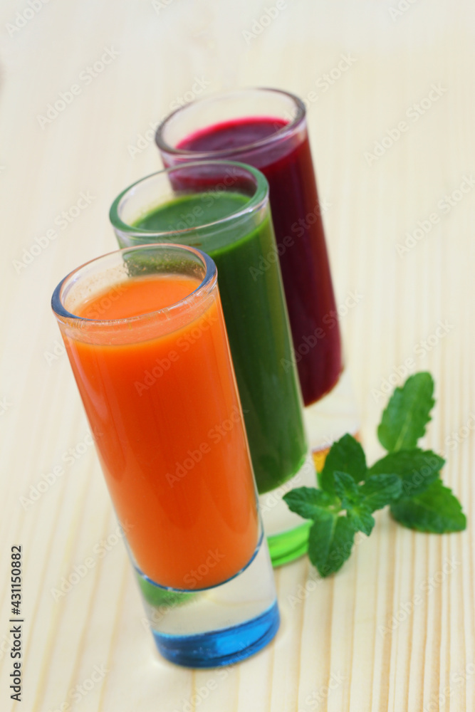 Carrot, spinach and beetroot smooties in transparent tall glasses on wooden surface
