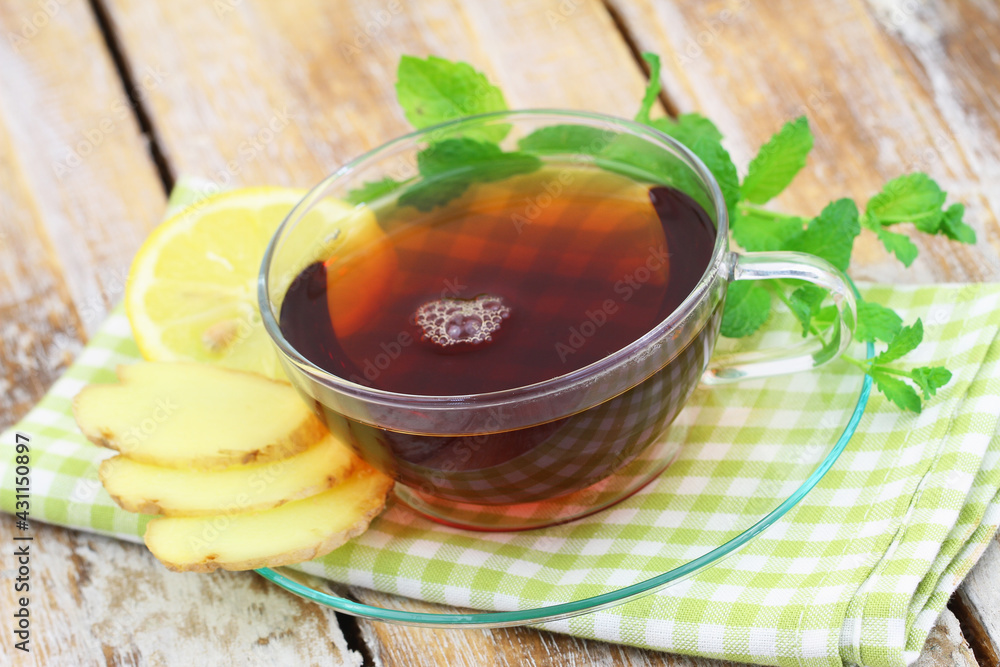 Organic tea in transparent cup, fresh mint leaves, slices of lemon and fresh ginger on rustic wooden surface