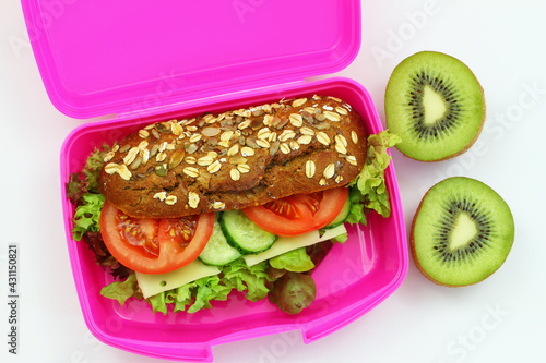 Brown sandwich and kiwi fruit in pink lunch box and kiwi fruit on white background shot from the top
