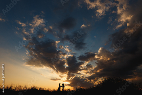 Man and woman are walking holding hands against the backdrop of a beautiful sunset sky