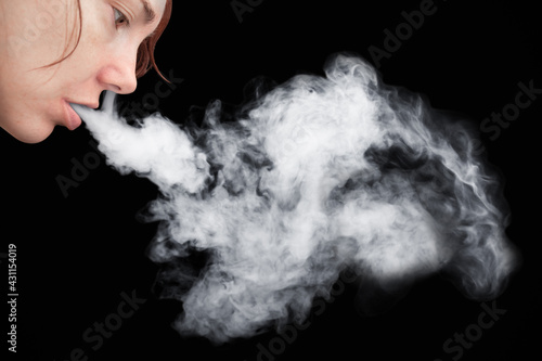 Face profile of young woman smoking with thick white smoke from mouth on black background.