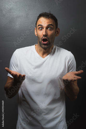 Man wearing a white tshirt over a grey background not understanding what is happening