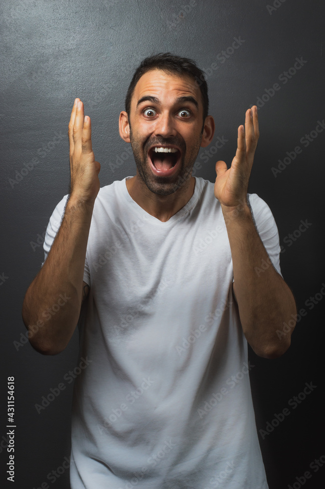 Man wearing a white tshirt over a grey background looking very surprised Man wearing a white tshirt over a grey background looking very surprised