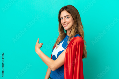 Super Hero caucasian woman isolated on blue background pointing back