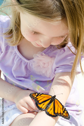 A little girl with a monarch butterfly on her arm
