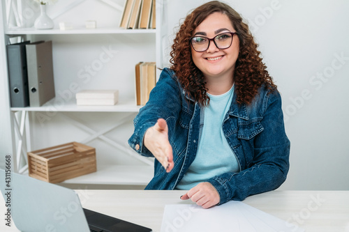 Greeting woman. Recruitment office. Job interview. Business meeting. Friendly communication. Smiling welcoming plus size lady in spectacles proposing hand shake on workplace.