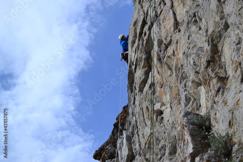 A rock climber in a white helmet climbs a rock in sunny weather