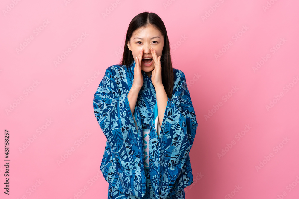 Young Chinese girl wearing kimono over isolated background shouting and announcing something Young Chinese girl wearing kimono over isolated background shouting and announcing something