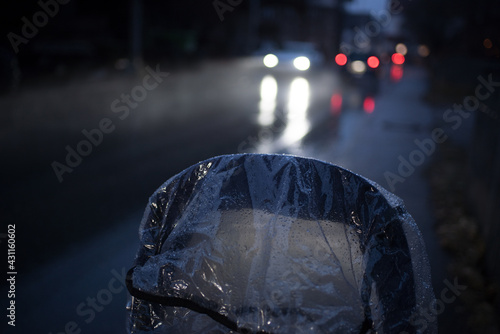 Kinderwagenverdeck mit Regenschutz bei Regen in Dunkelheit, Beleuchtung von entgegenkommenden Autos spiegelt sich im nassen Asphalt photo