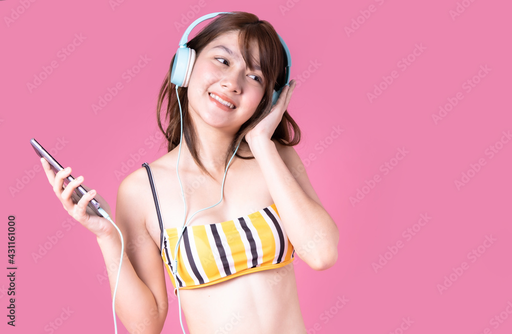 Beautiful,Sexy asian girl standing on pink background .She wear bikini and smiling.Summer vocation happy trip concept.mixed race woman listen music. Beautiful,Sexy asian girl standing on pink background .She wear bikini and smiling.Summer vocation happy trip concept.mixed race woman listen music.